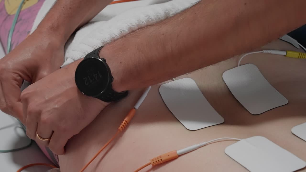 white electrodes connected to wires on lower back of woman lying on treatment bed