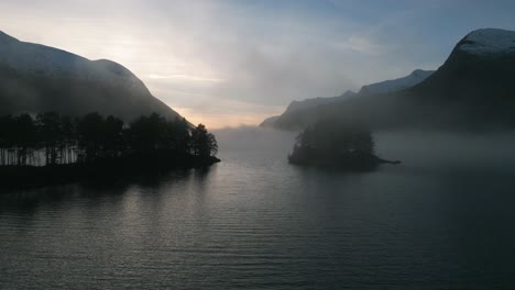 misty dawn over oppstrynsvatnet in norway with serene waters and mountain backdrop, aerial view