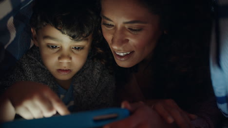 madre y hijo felices usando una tableta bajo una manta niño pequeño jugando juegos en tecnología de pantalla táctil con mamá relajándose divirtiéndose antes de acostarse
