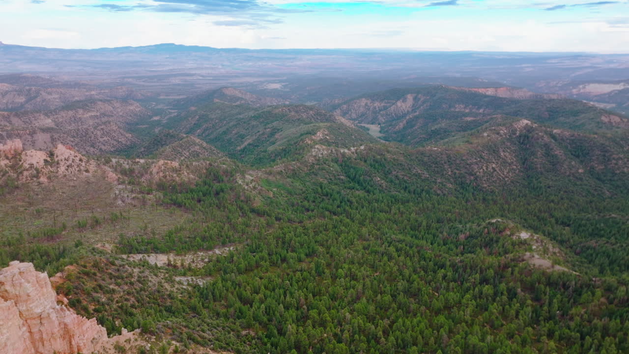 Mountainous panorama on cloudy daytime. Drone footage over the rocky landscape overgrown with pine tree forest.