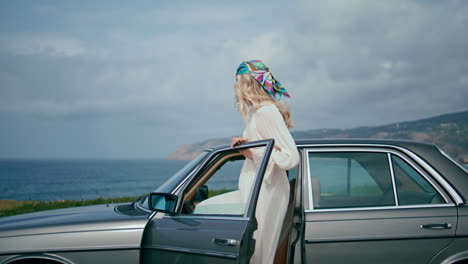 woman opening door car standing at cloud seashore. blonde sit down in retro auto