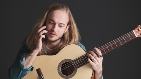 caucasian young man having a call while holding guitar.