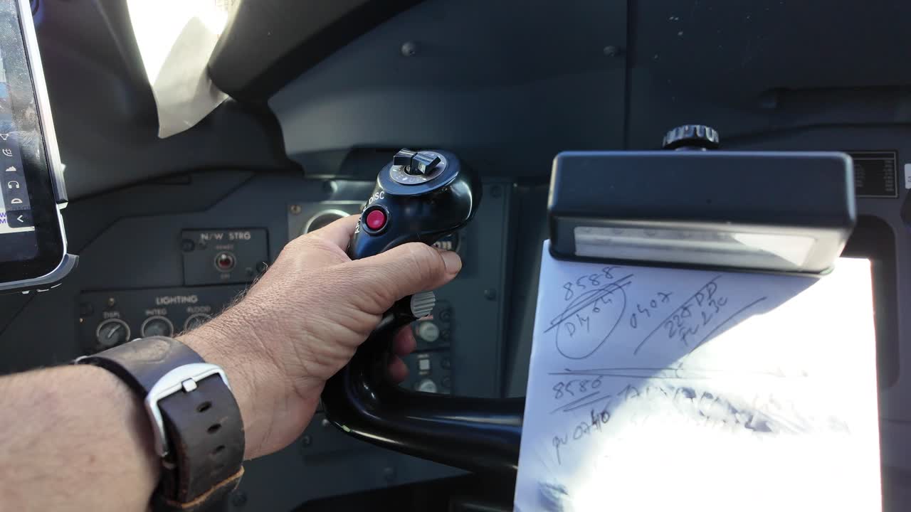 An extreme closeup view of the left hand of white pilot wearing a watch operating the control wheel inside the cockpit of a modern jet. Daylight. 4K 60FPS.