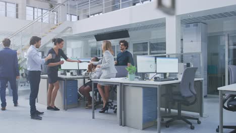 in the bright busy office group of young professionals have team building meeting. standing at the desk, discuss problem solutions, planning and strategizing, use digital tablets and desktop computers