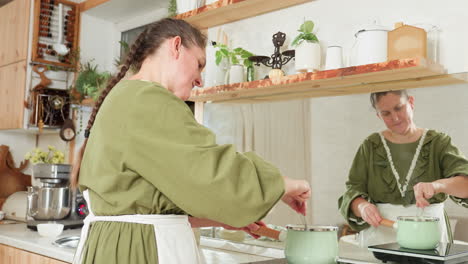 student cooks in modern kitchen while stirring food in pastel green pot on electric stove, steam rising as she watches reflection in mirror, focused on culinary task in cozy indoor setting