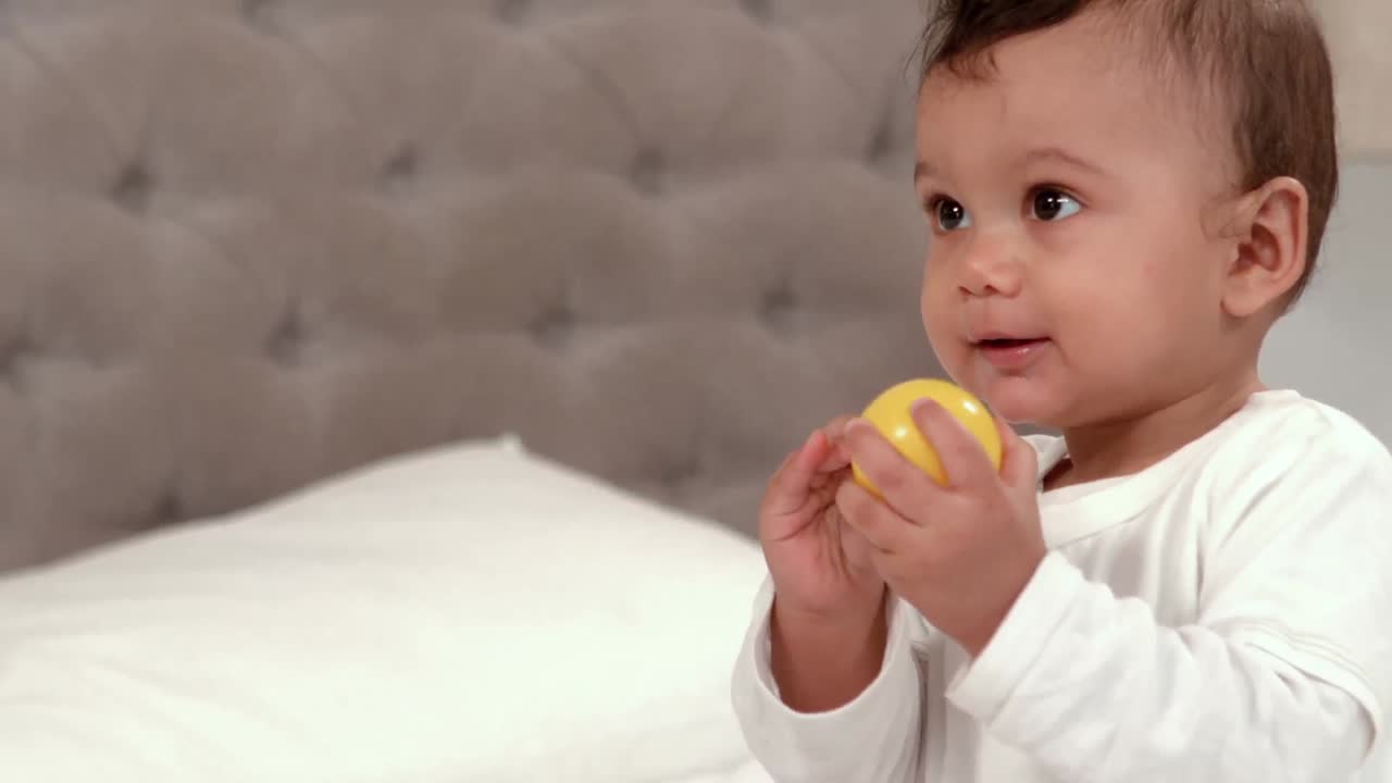 Cute baby playing with ball on bed