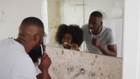 African-american-daughter-and-her-father-looking-in-mirror-brushing-teeth-together-in-bathroom
