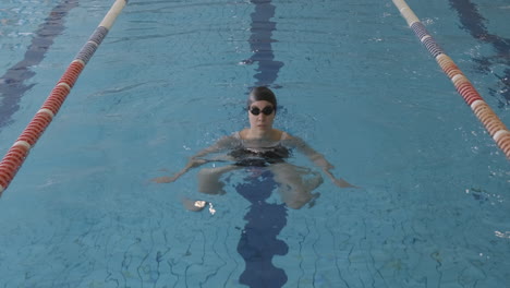 a young female swimmer does immersion exercises in an indoor swimming pool