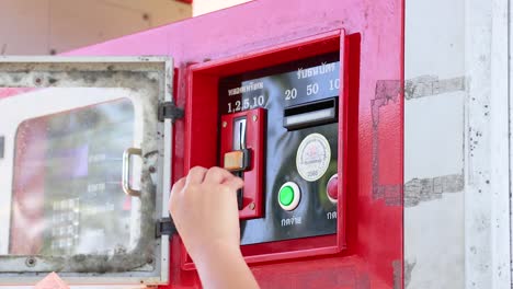 A person inserts cash into a red coin-operated fuel dispenser under bright daylight at Khao Rang Viewpoint, Phuket