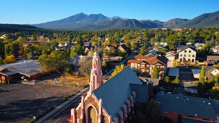 Edificio storico di spicco della Cappella della Natività della Beata Vergine Maria. Prospettiva aerea sulla città verde e sulle montagne verdeggianti in una giornata di sole. Flagstaff, Arizona, USA