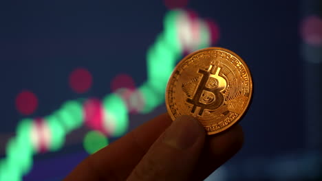 close up shot of man holding golden bitcoin with bullish candlestick chart in the background