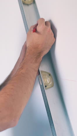 cu: upset young man in blue shirt and protective glasses checks wall level with modern instrument at room renewal closeup