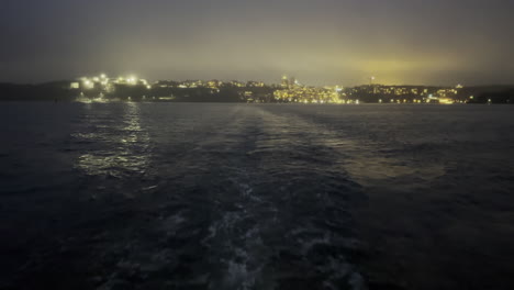 traveling by boat during night time with the city lid up in the horizon behind the boat