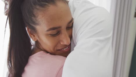 Video-of-happy-diverse-couple-smiling-and-embracing-by-window-at-home