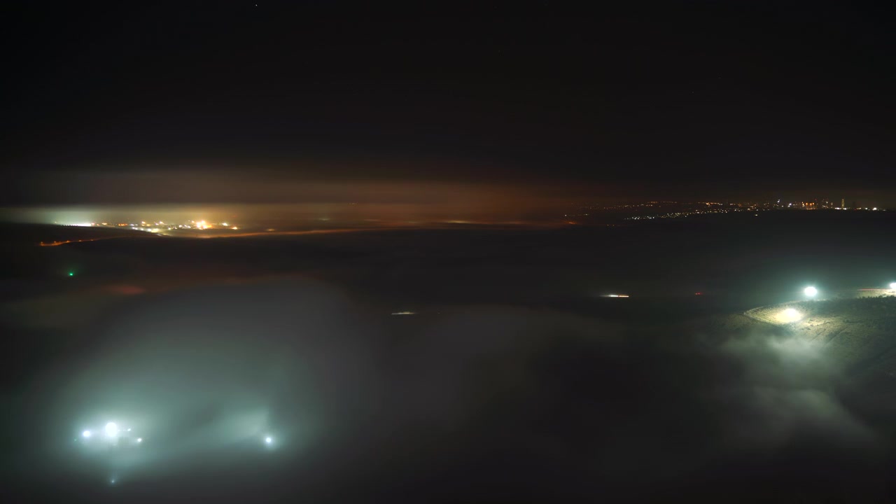Time Lapse of Night Fog Rolling Over Illuminated Landscape