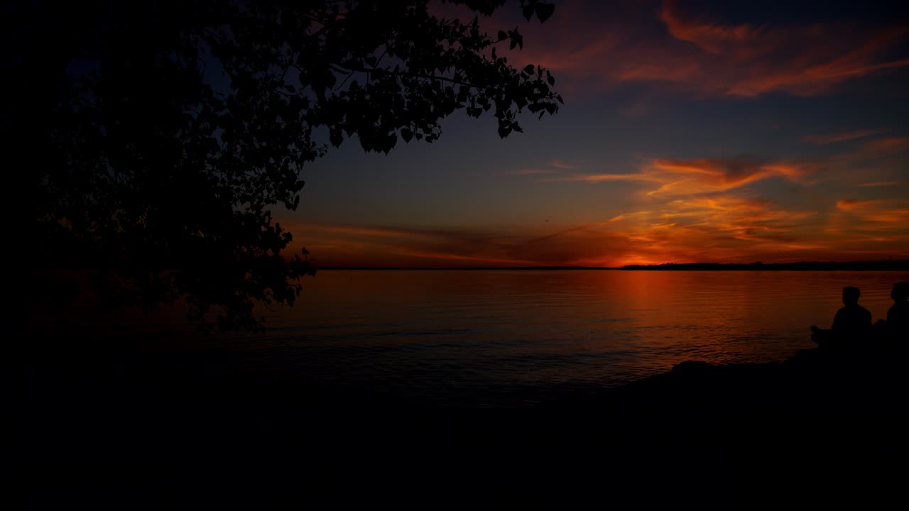 Zeitraffer eines orangefarbenen Sonnenuntergangs hinter der Silhouette eines Baumes am Britannia Beach, Ottawa.