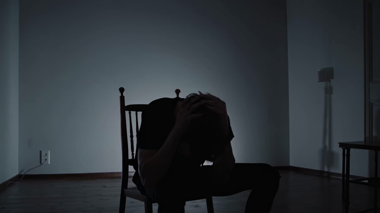 A moody video scene with a silhouette of a person sitting on a chair, head in hands