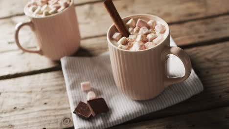 video of mugs of chocolate with marshmallows, decorations and copy space on wooden background