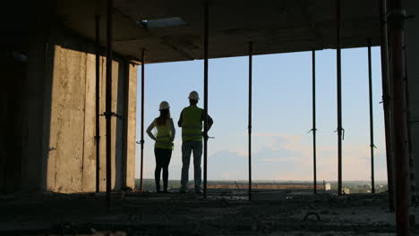 Builders-look-at-a-cityscape-on-a-sunset-background-back-view.