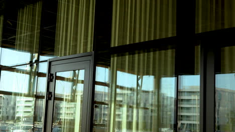 Interior-view-through-a-glass-curtain-wall-with-golden-reflections,-overlooking-other-buildings