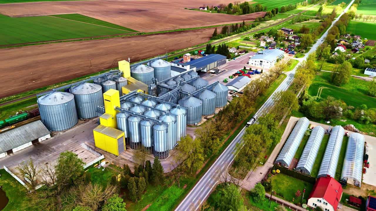 Large grain silos and greenhouses on farmland, spring day, aerial view