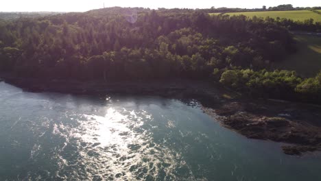 Luftaufnahme-über-Dem-Schäumenden,-Funkelnden-Sonnenuntergangsfluss,-Der-Entlang-Der-Waldlandschaft-Der-Menai-Straße-Fließt