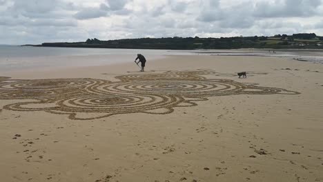man creëert artistieke vloeiende patronen op het zandige angelsey strand met zijn terrier hond