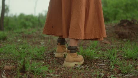 Woman-in-orange-skirt-and-boots-walking-through-a-grassy-field