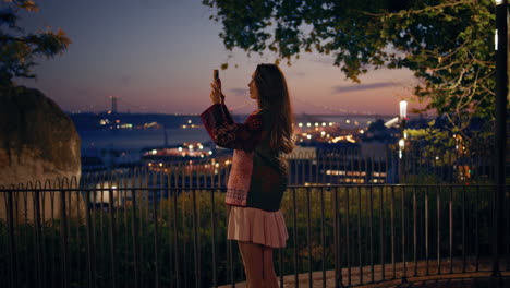 girl recording night city video on smartphone standing observation deck railings