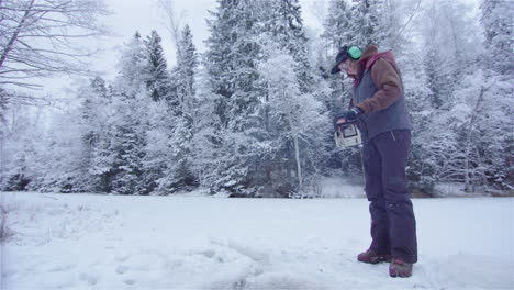 woman with chainsaw starts the engine and prepares to cut an ice hole