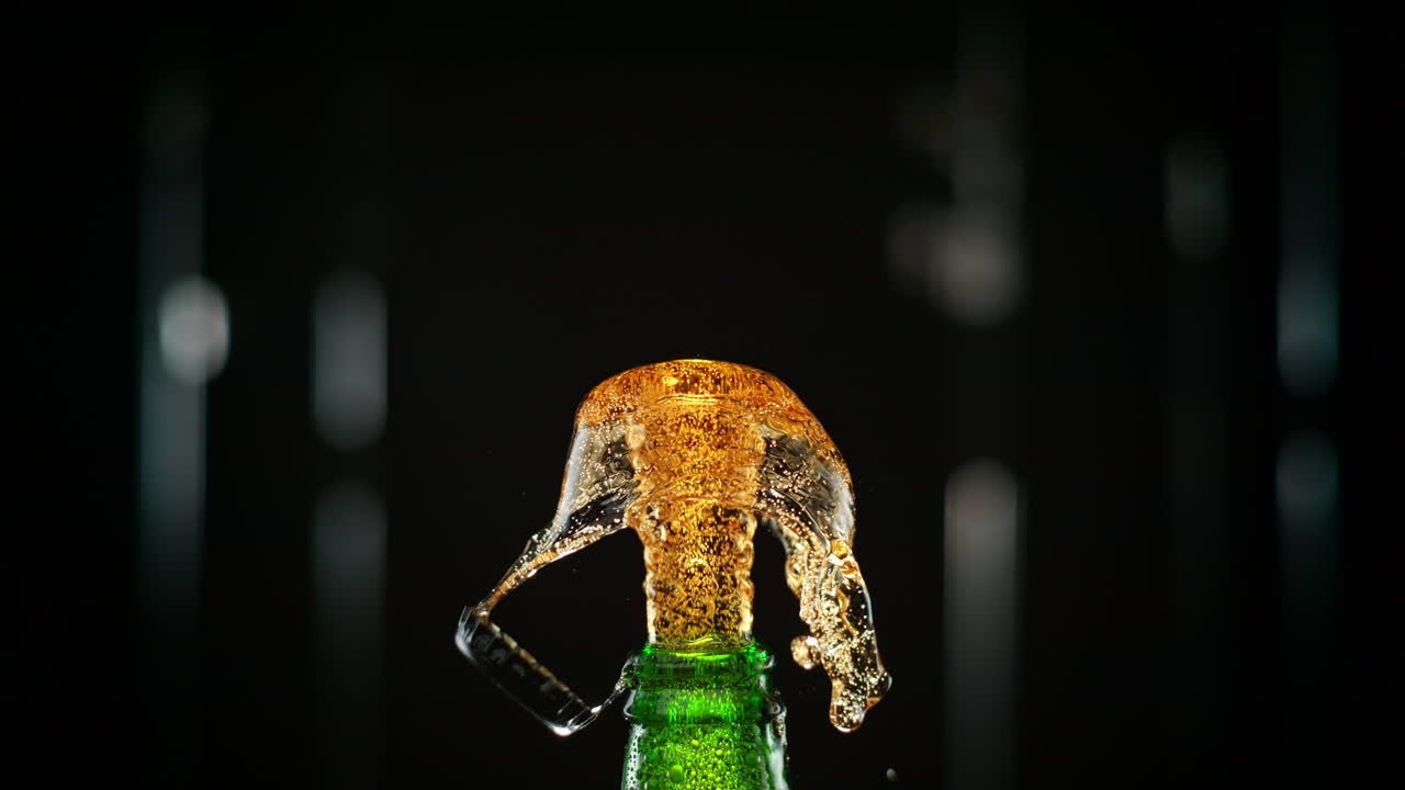 Cap Pops Off A Green Bottle, And Carbonated Beer Erupts In A Golden Stream in Slow Motion