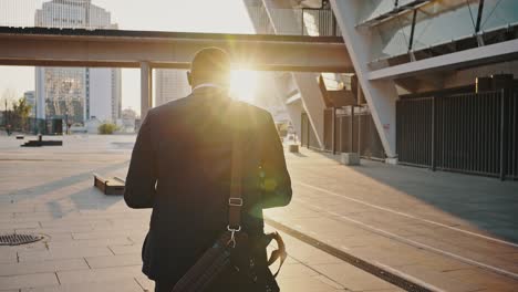 back view of confident african american businessman going in business area to sunset, looking at watch on hand