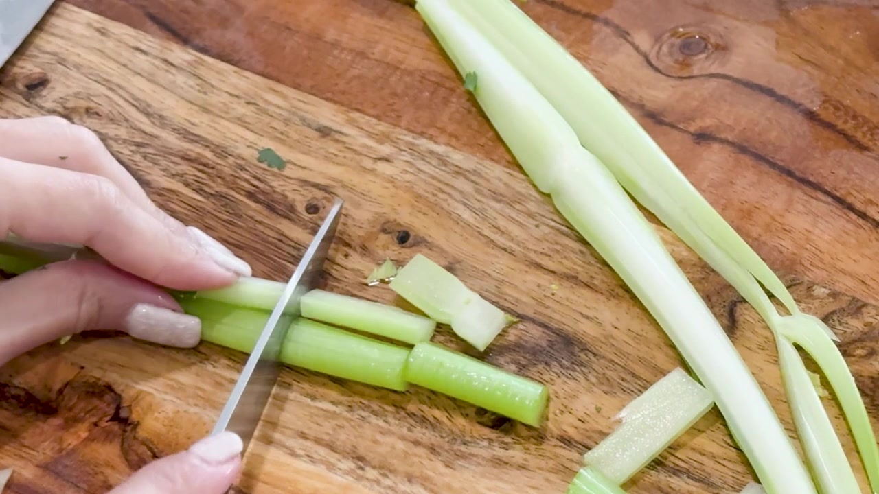 Una vista dall'alto mostra delle mani che usano un coltello per tagliare a pezzi gambi di sedano verde