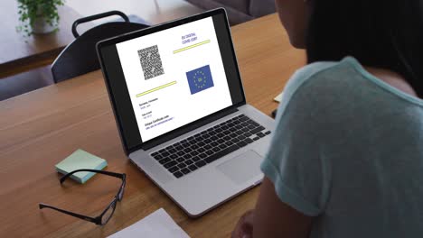 Woman-working-at-desk,-covid-vaccination-certificate-with-qr-code-and-eu-flag-on-laptop-screen