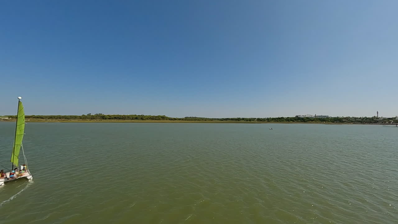un rápido zoom aéreo más allá de un catamarán velero bajo vela en aguas fangosas