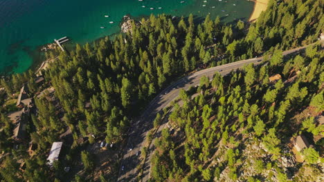highway in the pine tree forest with few cars on. shore of the blue lake with numerous boats on. aerial view.