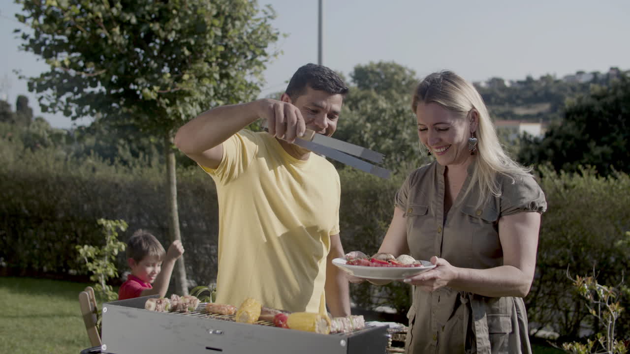 Uomo sorridente che mette kebab e verdure nel piatto della moglie