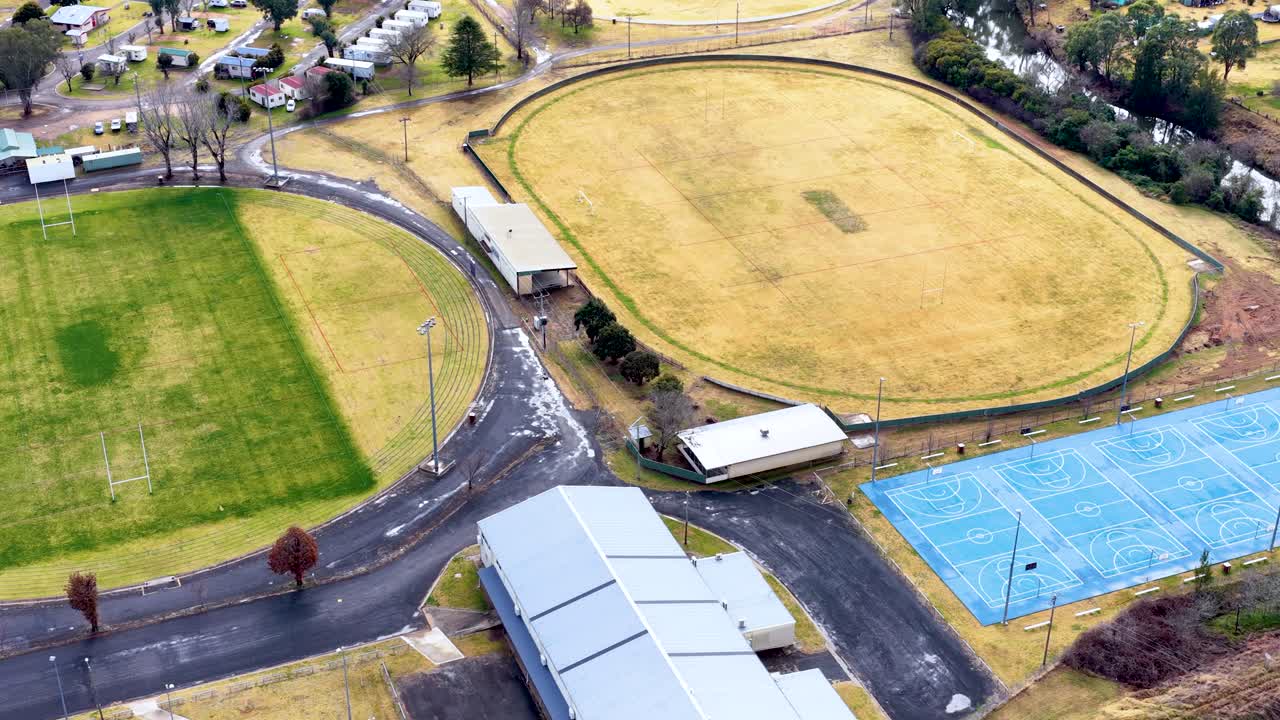 Aerial view of an oval sports field in Coonabarabran, Australia, showing rapid transition from dry yellow grass to lush green turf under consistent daylight