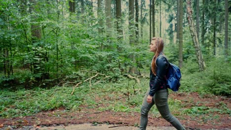 a girl with a backpack walks through the forest on a path in slow motion