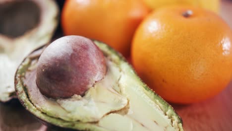 Close-Interior-Shot-of-Clementines-Spinning-Right-to-Reveal-the-Avocado-Stone-in-a-Half-Avocado-followed-by-the-other-half-on-Wooden-Surface