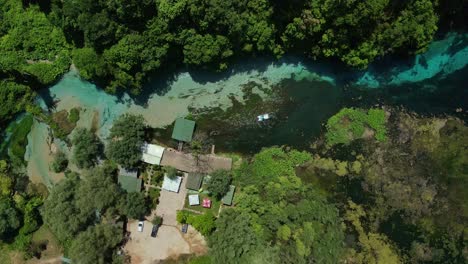 Aerial-overhead-lowering-onto-boat-moving-along-blue-eye-spring,-Albania