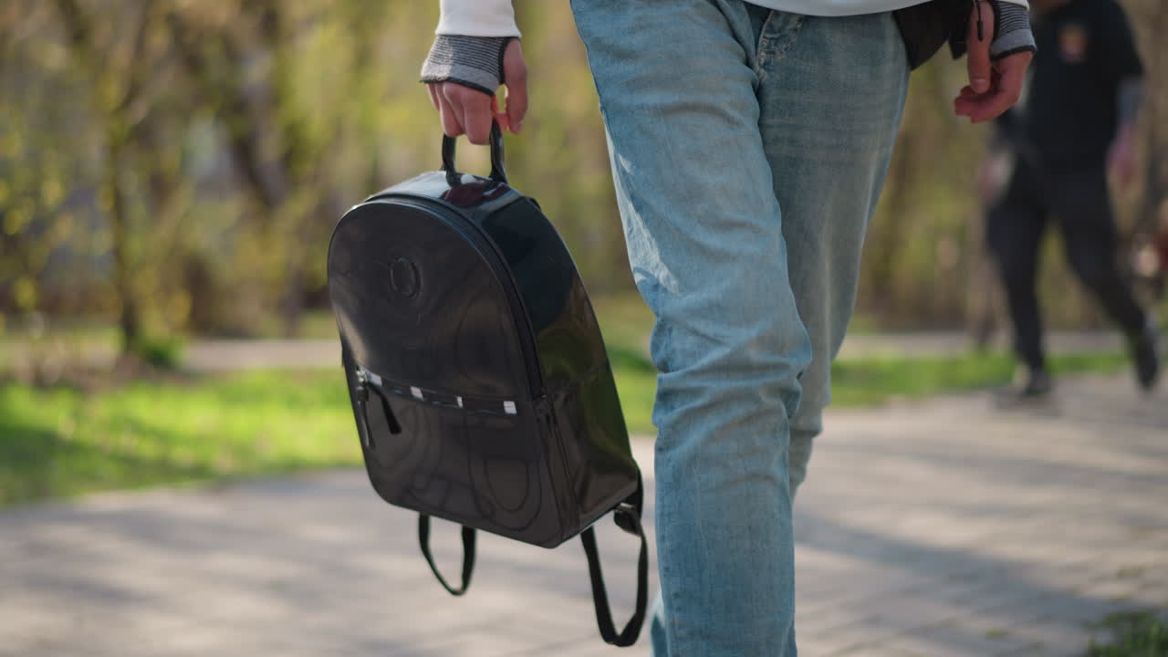 peatón con mochila, persona informal con una mochila negra caminando por el sendero del parque, peatón con ropa informal paseando por el sendero del parque con una mochila negra grande a la luz de la primavera