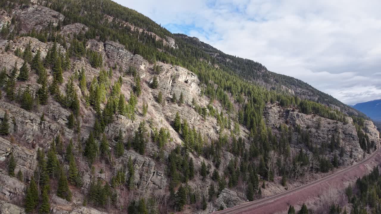 Vista aerea con drone di una collina rocciosa e boscosa e di un pendio montano con alberi sempreverdi e una strada alla base, vicino alla valle del fiume Flathead a Whitefish, Montana