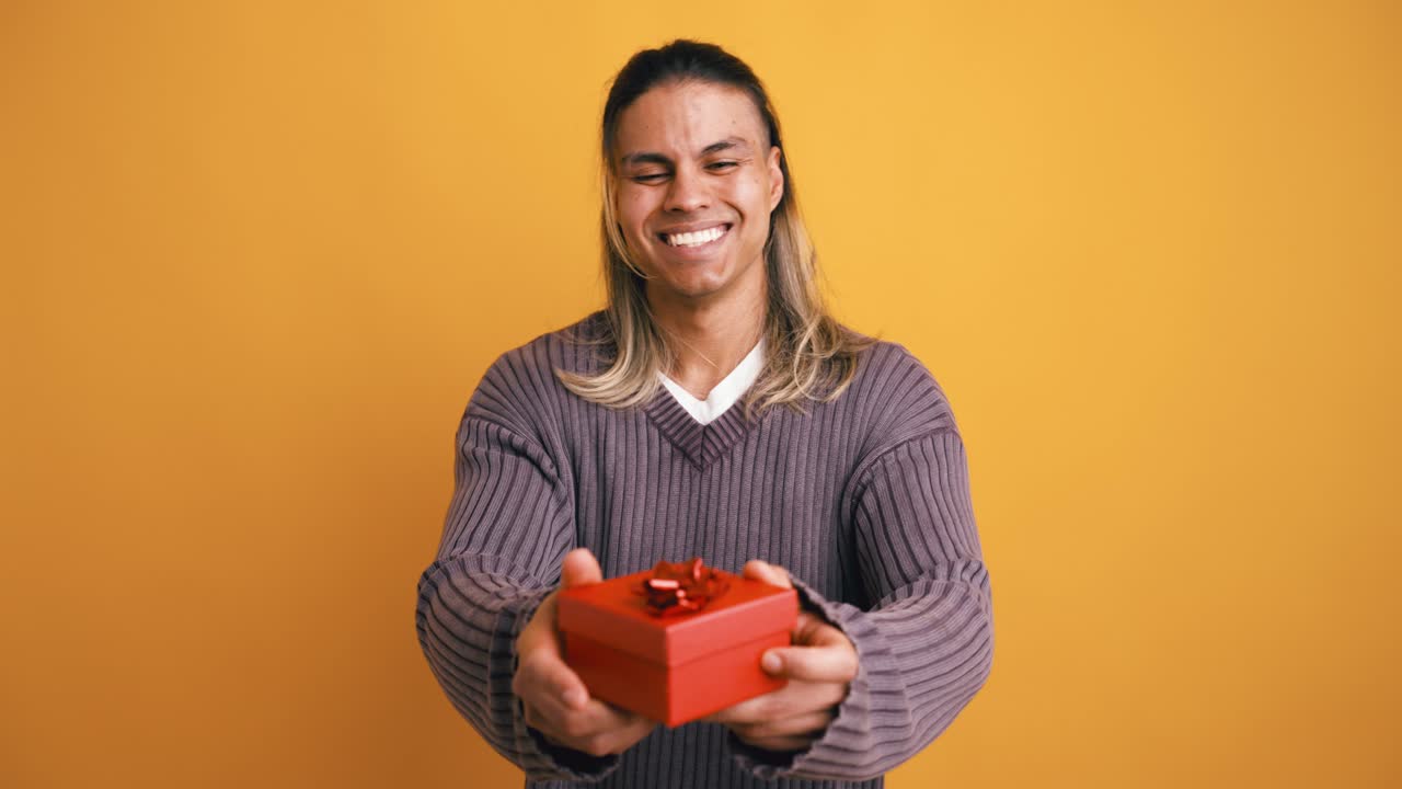 Giovane uomo sorridente che presenta una scatola regalo rossa