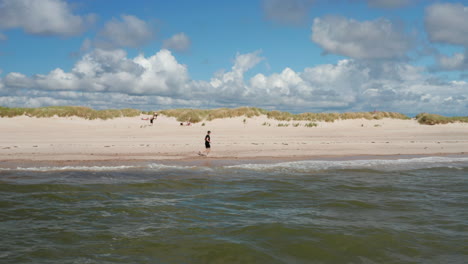 Menschen,-Die-Einen-Sonnigen-Tag-Am-Sandstrand-Genießen.-Sportler,-Der-Entlang-Milder-Wellen-Läuft,-Die-Küste-Waschen.-Ort-Für-Sommerferien.-Dänemark