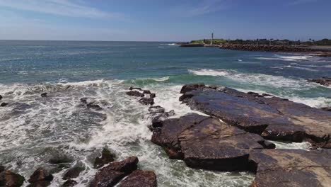 the splash of surf over wet rocks with two light houses and wollongong harbour beyond