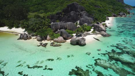 pull back aerial of boulders kayaker and palm trees on popular seychelles beach on la digue island