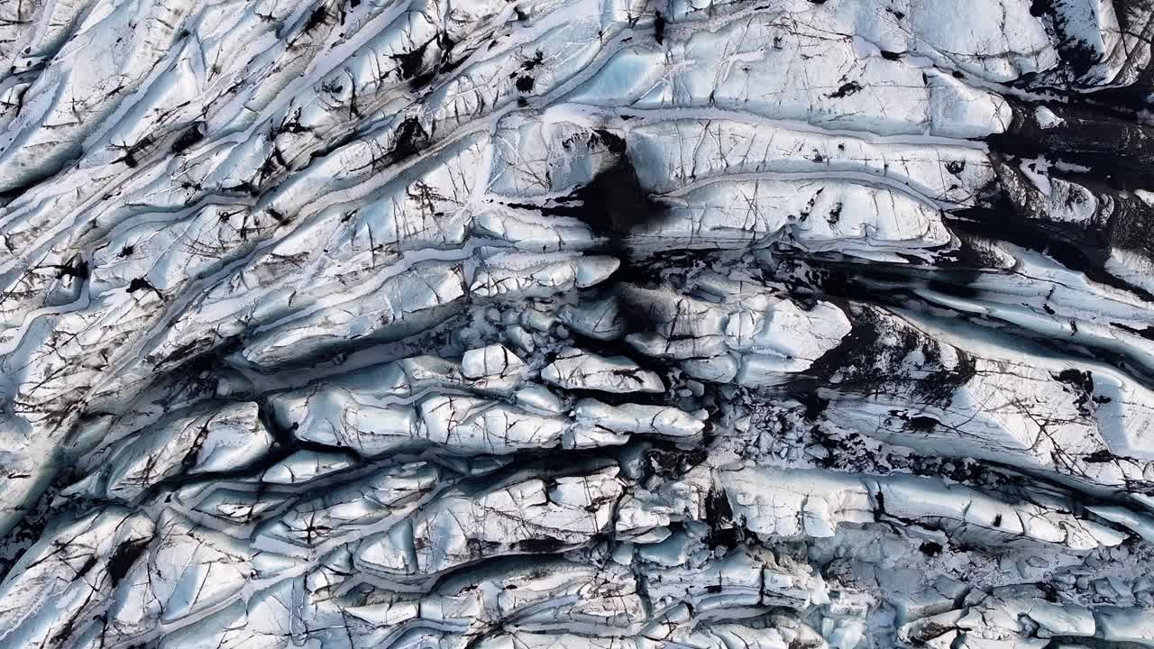 Aerial drone close-up of Solheimajokull glacier ice textures, deep crevasses, black volcanic ash lines, stunning view of climate change impact on glaciers.