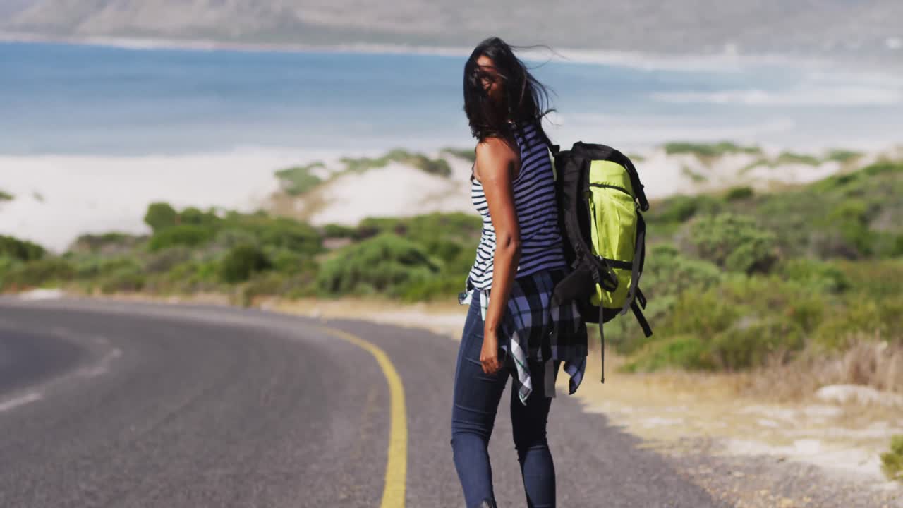 mujer afroamericana con mochila tratando de atrapar un ascensor mientras camina por la carretera