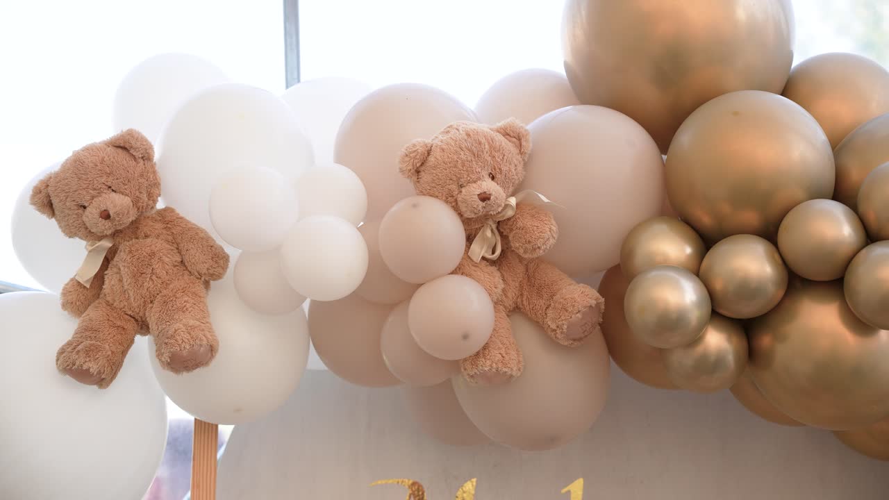 Cute teddy bears nestled in clusters of gold, beige, and white balloons, creating a soft and elegant party decoration perfect for baby showers or children's birthday celebrations